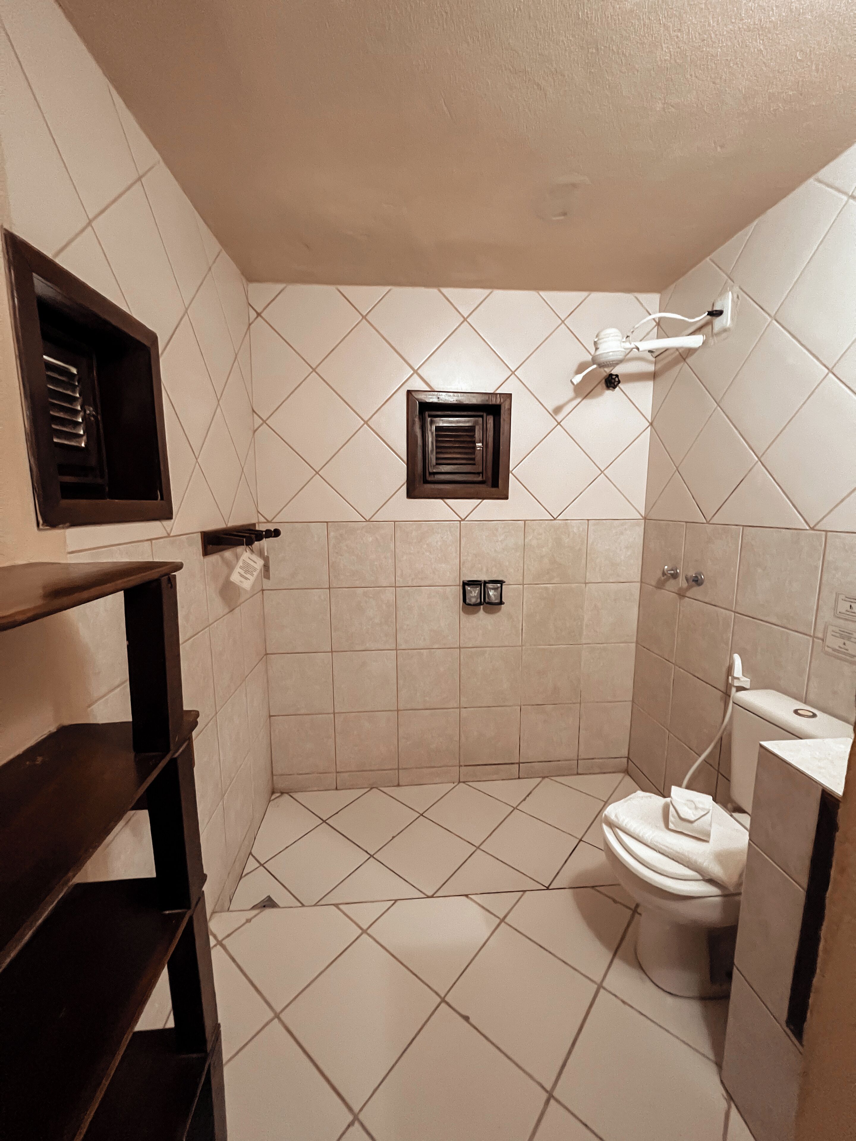 A small, tiled bathroom with a toilet, a shower area, and a towel rack.