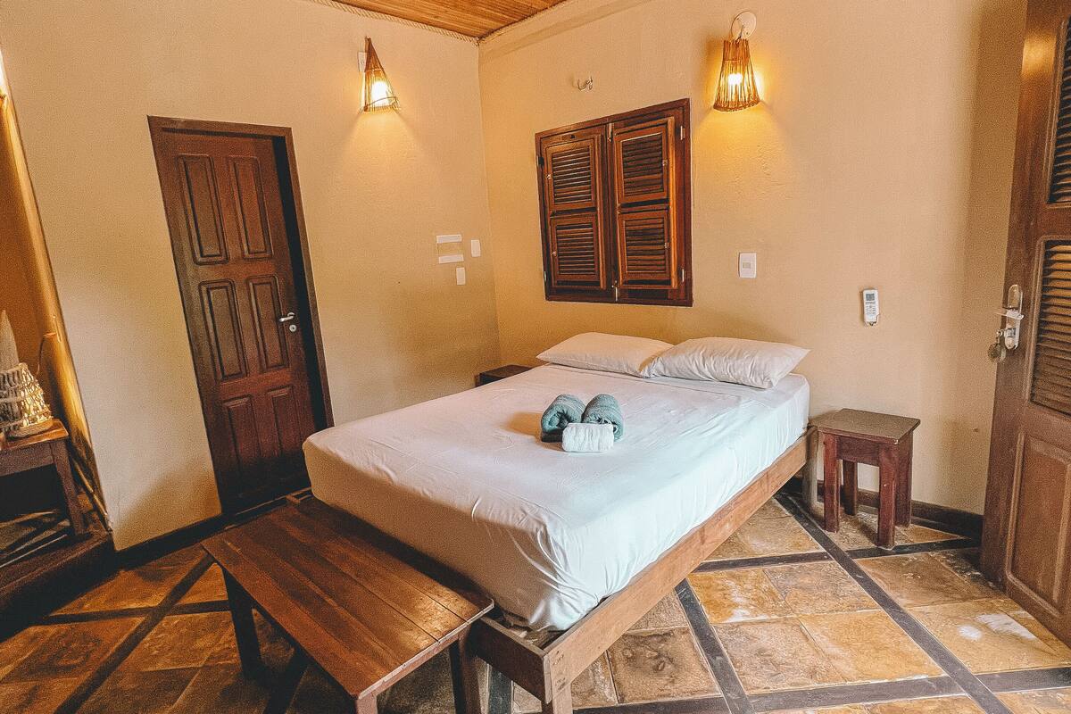 Un dormitorio con una cama de madera, un banco, una mesita y una puerta.