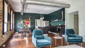 A modern living room with teal armchairs, a dining area, and a kitchen.