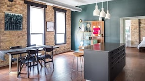 A modern kitchen with a central island, a dining area with chairs, and a bar area with a shelf and hanging lights.