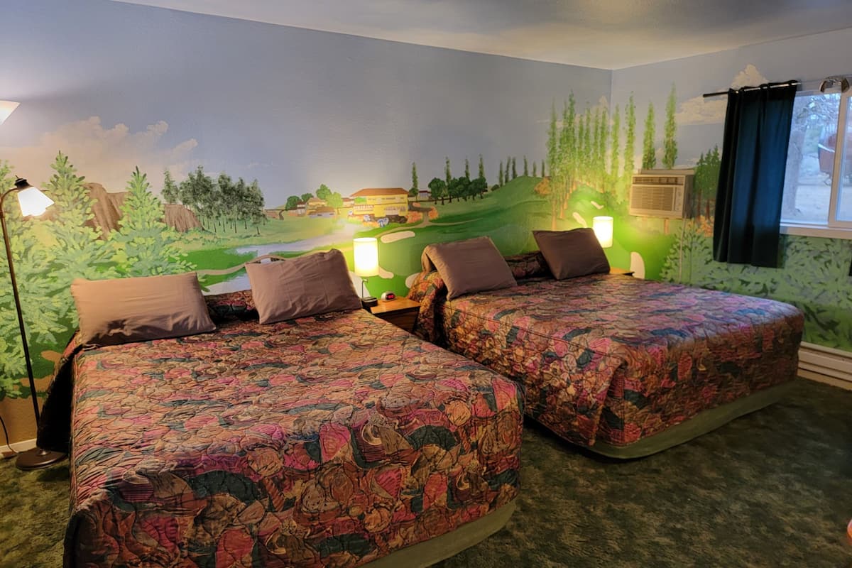 A room with two beds, each with floral-patterned bedding, a mural of a landscape on the wall, and a window with curtains.