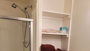 A bathroom with a shower, toilet, and shelves with towels. - La Collage Inn (Odessa)