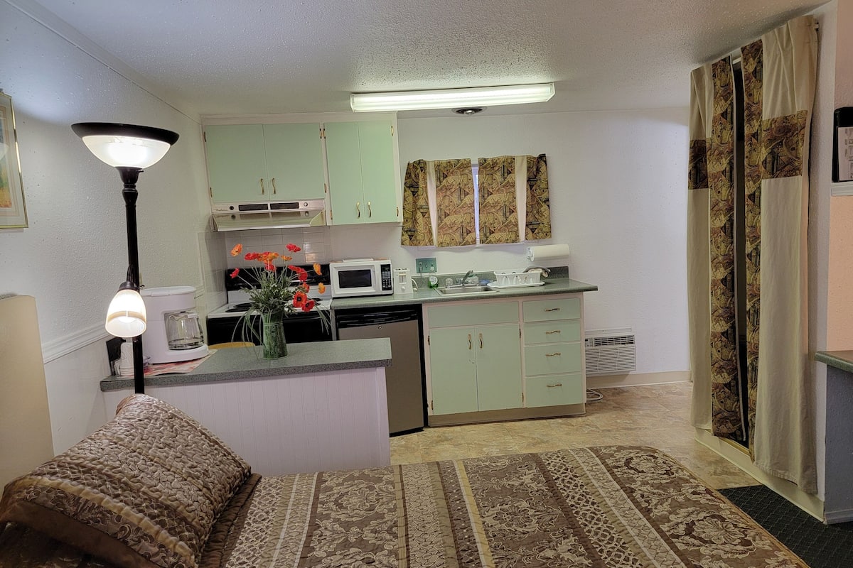 A compact kitchen with a microwave, sink, and green cabinets.