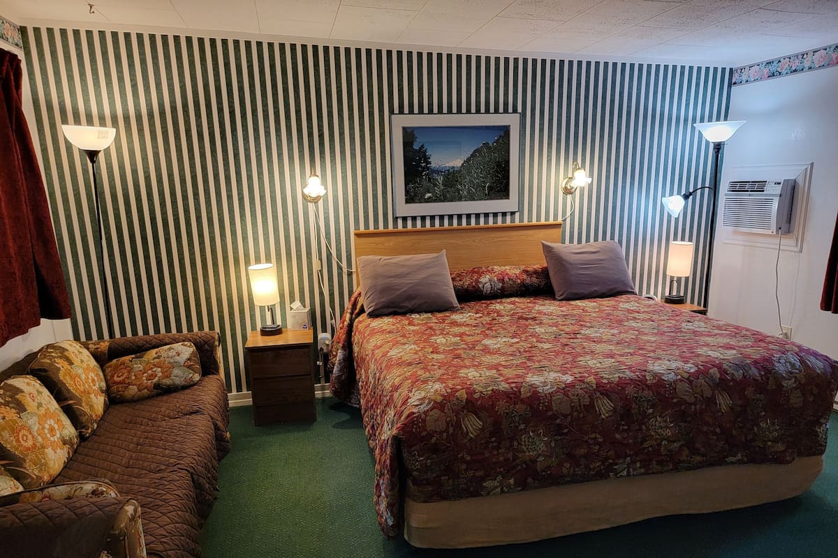 A hotel room with a large bed, two bedside tables with lamps, a couch, and a framed picture on the wall.