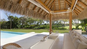 A poolside area with a thatched roof, a sofa, and a dining table.