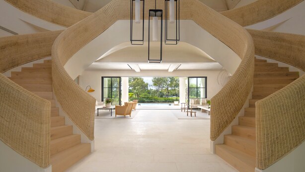 A spiral staircase with a woven handrail and pendant lighting, leading to a spacious area with a view of greenery outside.
