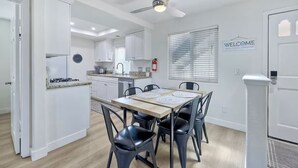 A modern kitchen with white cabinets, a dining table with black chairs, and a ceiling fan. - Cozy 2-bedroom condo with WiFi, AC in peaceful Oceanside (Oceanside)