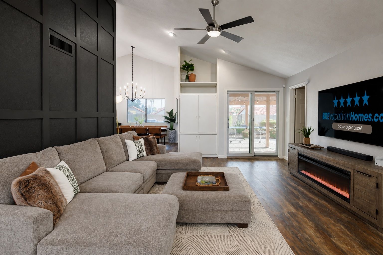 A modern living room with a sectional sofa, a flat-screen TV, a fireplace, and a ceiling fan.