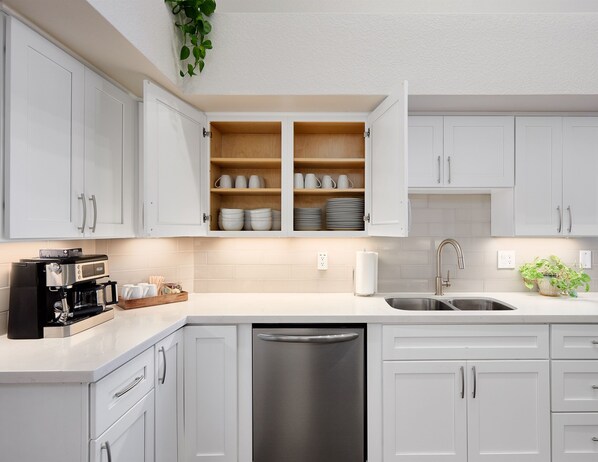 A modern kitchen with white cabinets, a stainless steel dishwasher, and a coffee maker. - Resort Backyard: Heated Pool, Hot Tub, Fire Table, EV, 3 Primaries (Scottsdale)