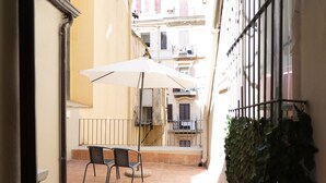 A narrow outdoor patio with a table and chairs under a large umbrella, surrounded by buildings with balconies and railings. - GG - Grow - Terrazza di Bellavista (Naples)