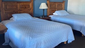 Een hotelkamer met twee bedden, houten hoofdborden, een nachtkastje met een lamp en een stoel.