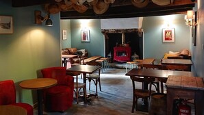 Un restaurante acogedor con mesas y sillas de madera, una chimenea y sombreros colgando del techo.