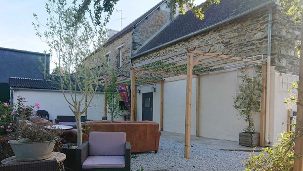 Un patio con mobiliario de mimbre, una pérgola de madera y un edificio de piedra.