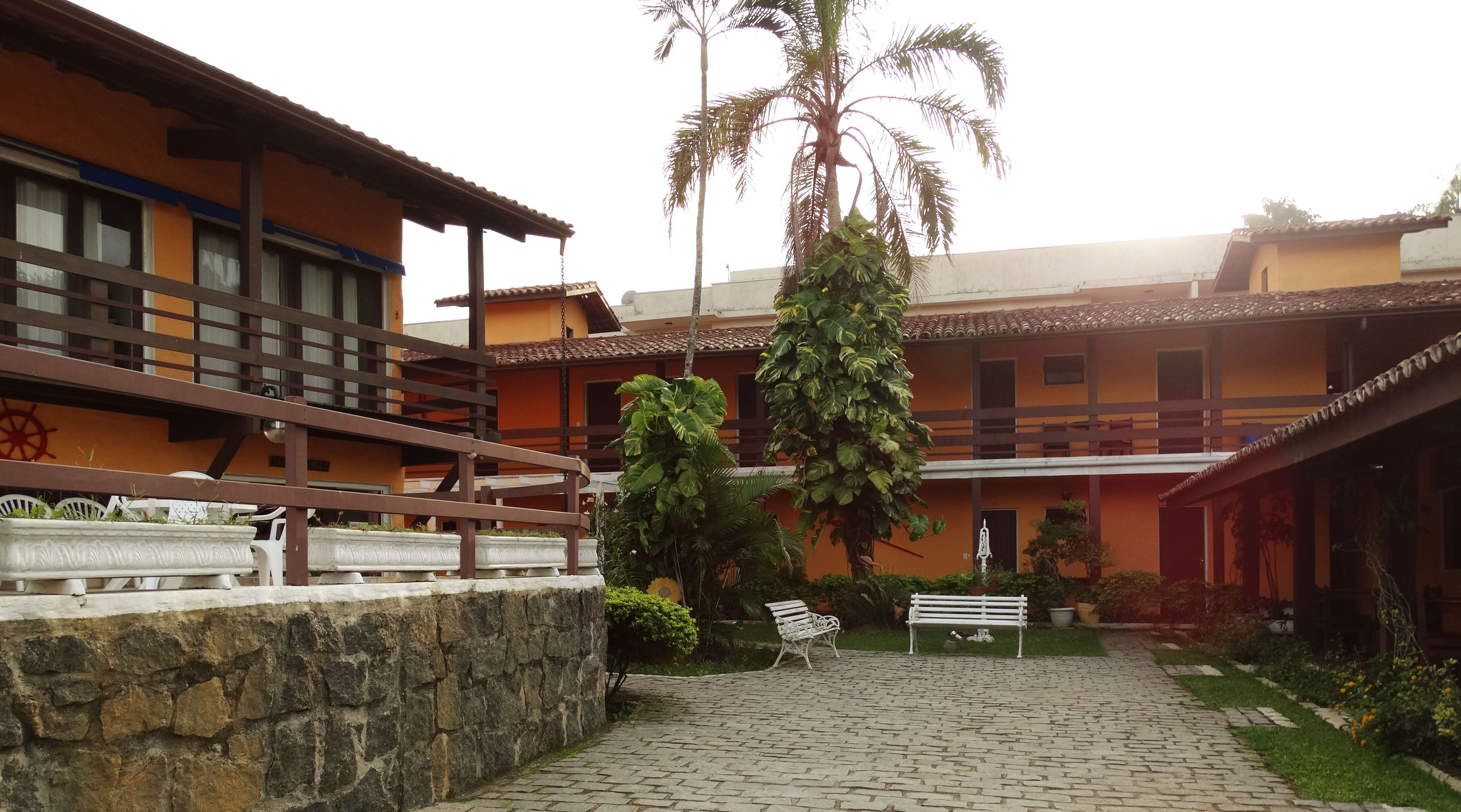 A courtyard with stone flooring, a white bench, and a palm tree.