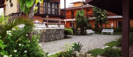 A courtyard with a stone pathway, white benches, and lush greenery.