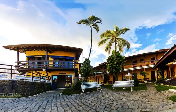 A building with a curved roof, a balcony, and a stone wall. - Pousada do Sol (Ubatuba)