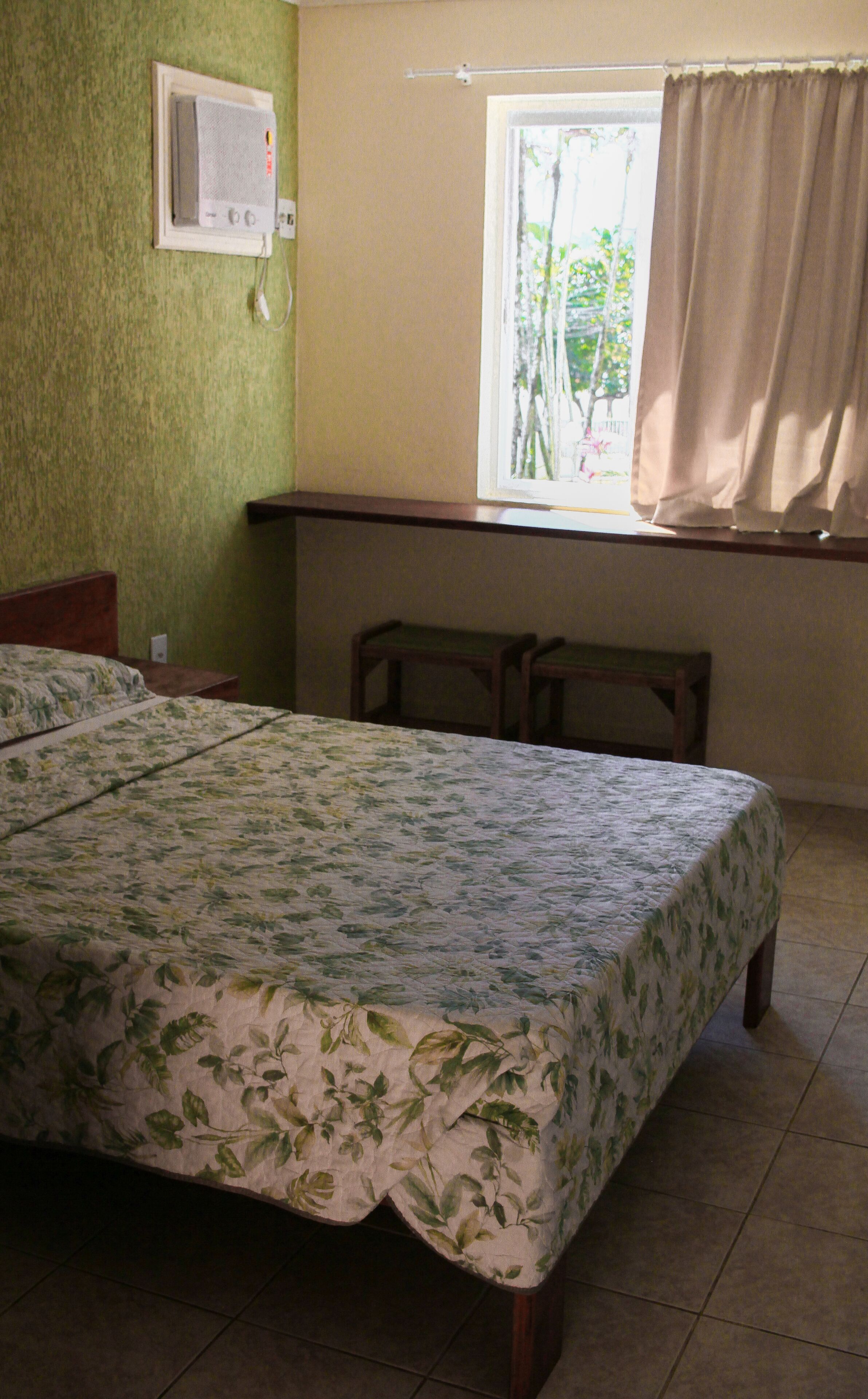 A bedroom with a bed, a window with curtains, a bedside table, and a wall-mounted heater.