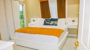 A hotel room with a large bed, white bedding, a golden throw blanket, and a nightstand with a lamp. - Cozy Luxury Hideaway With Free Wifi,Parking,Swimming Pool&Jacuzzi Near Negril 1b (Green Island)