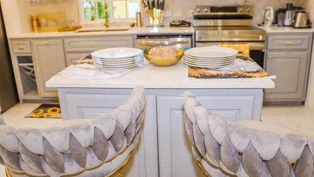 A kitchen with a marble countertop, a central island with plates and a bowl, and a view of the outdoors through the window. - Cozy Luxury Hideaway With Free Wifi,Parking,Swimming Pool&Jacuzzi Near Negril 1b (Green Island)