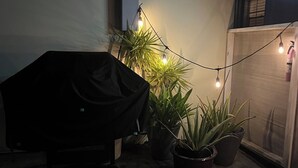 Een overdekte barbecue, planten in potten en lichtslingers in een achtertuin.