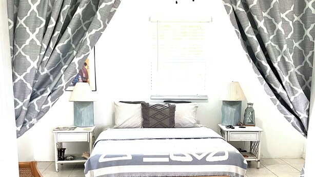 Een slaapkamer met een bed, twee nachtkastjes, een houten bankje, een vloerkleed en gordijnen.