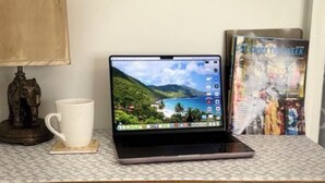 Een laptop op een plank met decoratief behang, een witte mok en een decoratief olifantje.