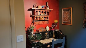 Ein Zimmer mit roter Wand, einem dekorativen Regal mit verschiedenen Gegenständen, einem gerahmten Kunstwerk und einem Tigerteppich.
