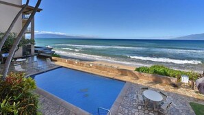 Ein Poolbereich mit Blick auf den Ozean, Sitzgelegenheiten im Freien und ein Gebäude mit einem Balkon.