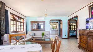 Ein geräumiges Wohnzimmer mit einer Couch, einem Couchtisch und einem Fernseher. Es gibt große Fenster und eine Steinwand.