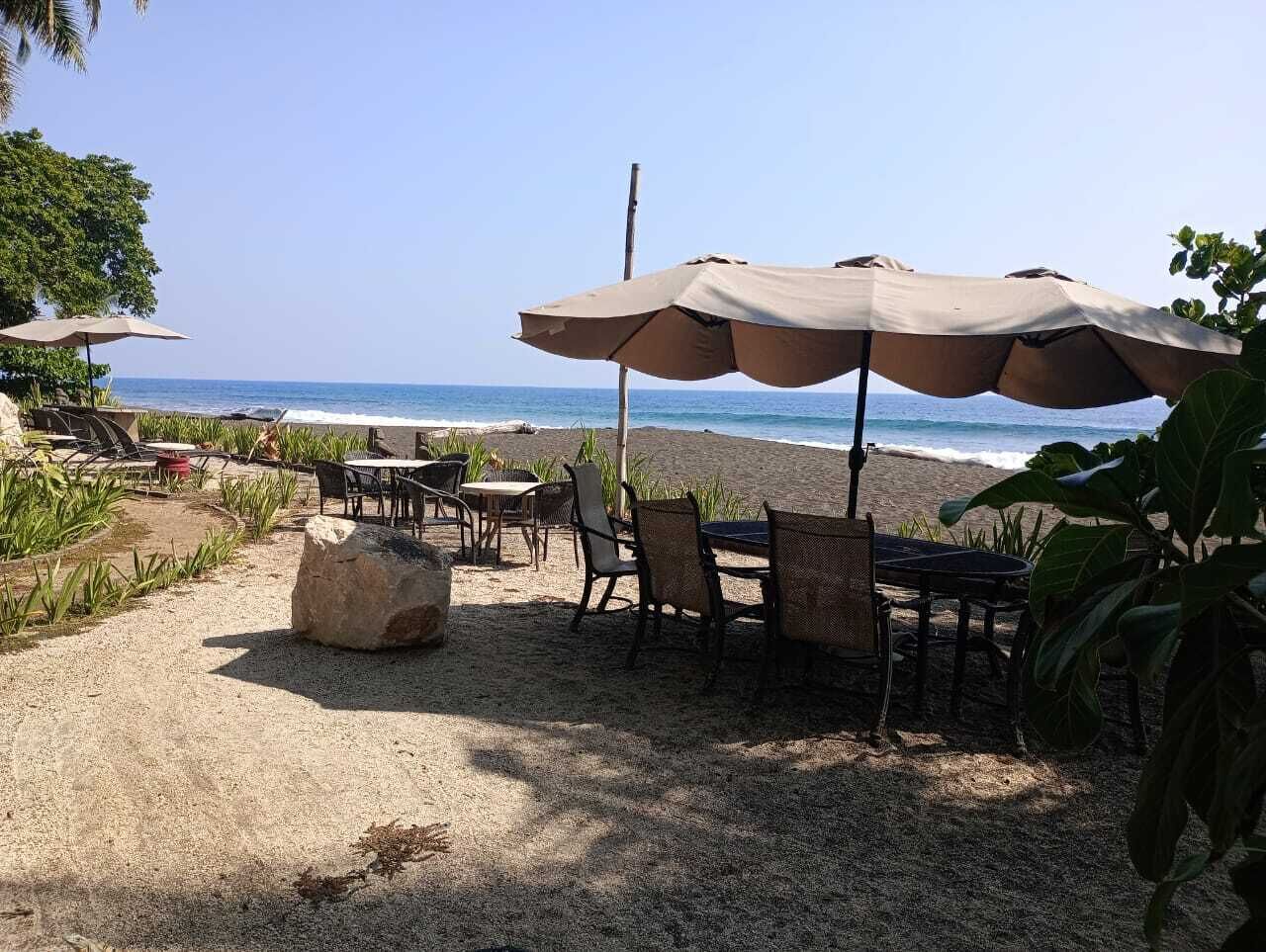 An outdoor seating area with tables and chairs, a large rock, and a beach view.