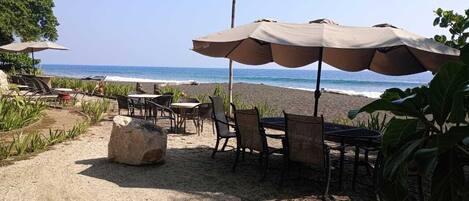 An outdoor seating area with tables and chairs, a large rock, and a beach view.