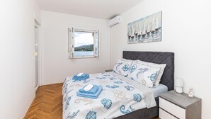 A bedroom with a bed, a nightstand, a window with a view of a landscape, and a painting of sailboats. - Lovely apartment in Marina with house sea view (Marina)