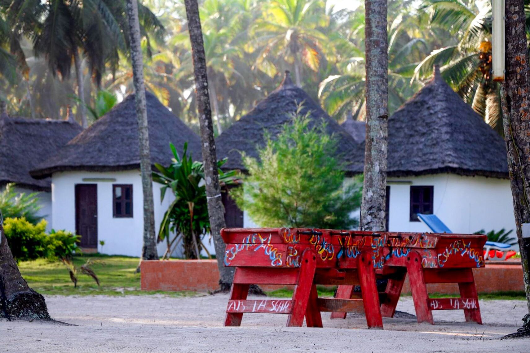 A row of thatched-roof huts with a bench in the foreground.