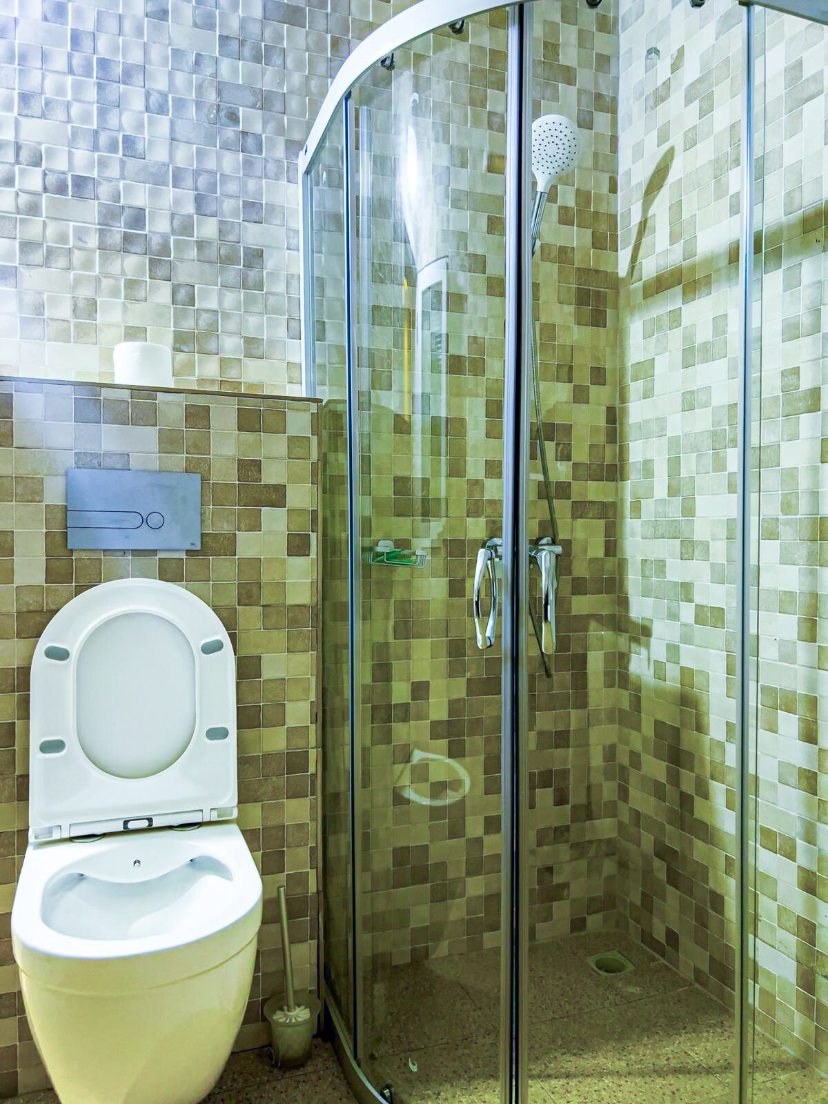 A bathroom with a toilet, a glass-enclosed shower, and tiled walls.