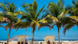 A beach with palm trees, a beach chair, and a small hut with a canopy. - Sabbat Plage (Mohamé)