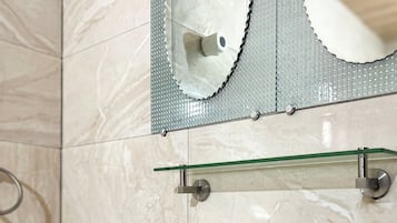 Een badkamer met een witte wastafel, een chromen kraan en een glazen plank erboven.