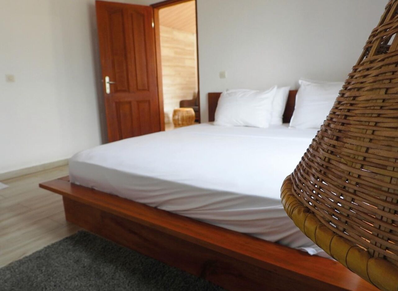 Une chambre à coucher avec un lit en bois, du linge de lit blanc et une chaise en osier.