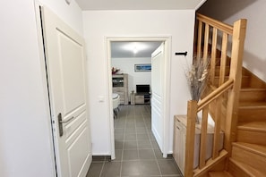 Um corredor com escadas de madeira, uma porta branca e chão de azulejos.