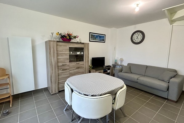 Um espaço compacto com mesa de jantar, sofá, televisão e relógio na parede.