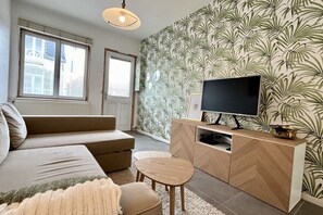 A living room with a sofa, a TV on a wooden stand, and a patterned wallpaper.