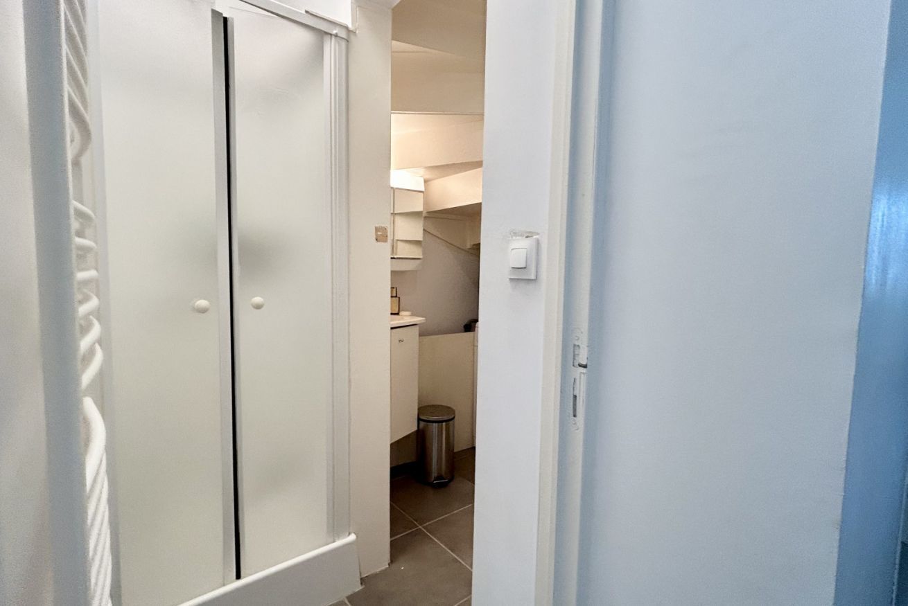 Un pasillo con una puerta cerrada, un cesto de basura y una lámpara al fondo.
