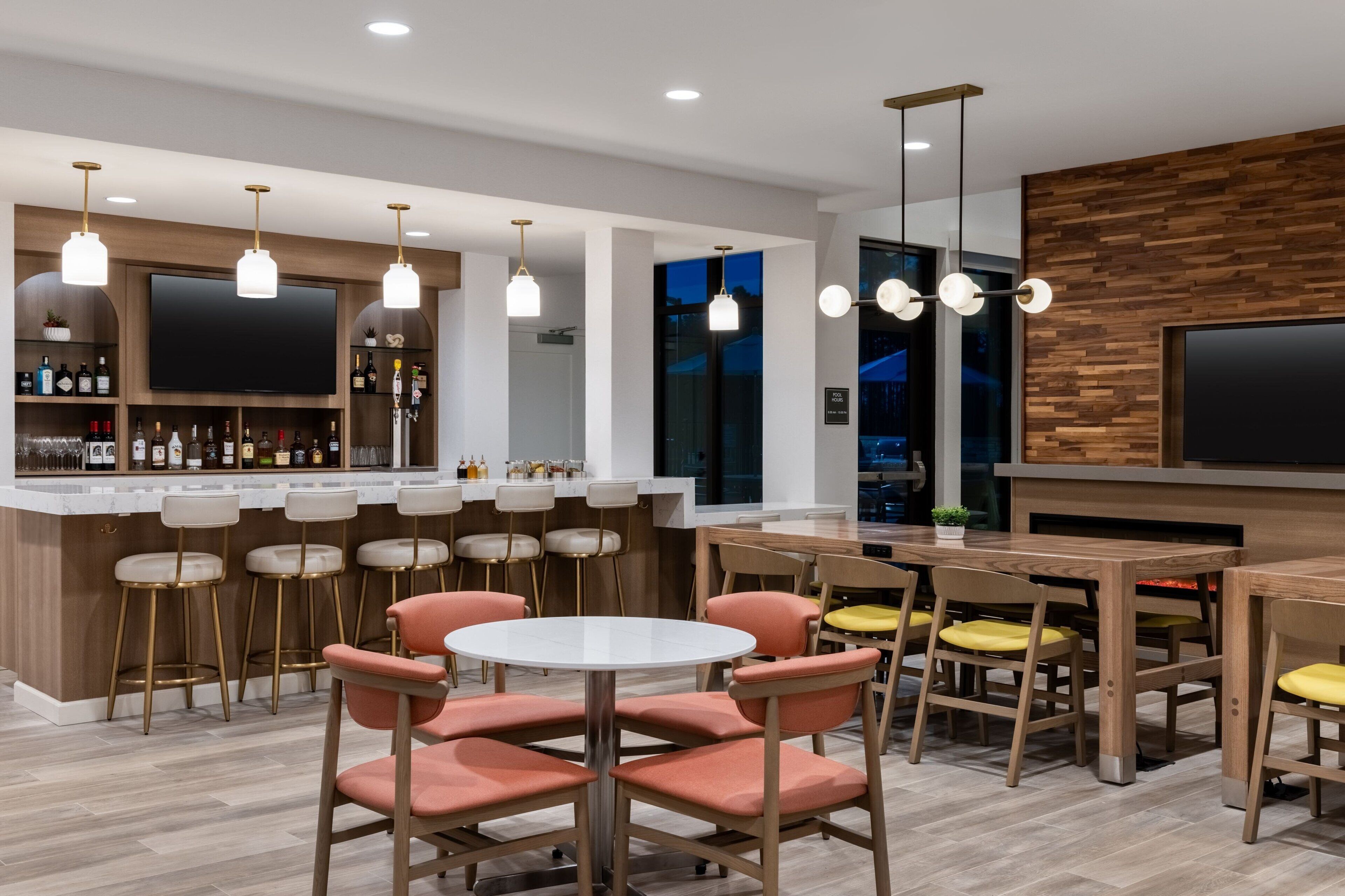 A modern bar area with a wooden bar counter, multiple stools, and a large flat-screen TV mounted on the wall.