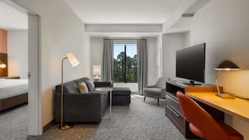 Une chambre d’hôtel avec un lit, un canapé, un bureau, une chaise, une télévision et une fenêtre avec des rideaux.
