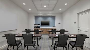 A conference room with a long table, six chairs, a flat-screen TV, a coffee station, and a whiteboard.
