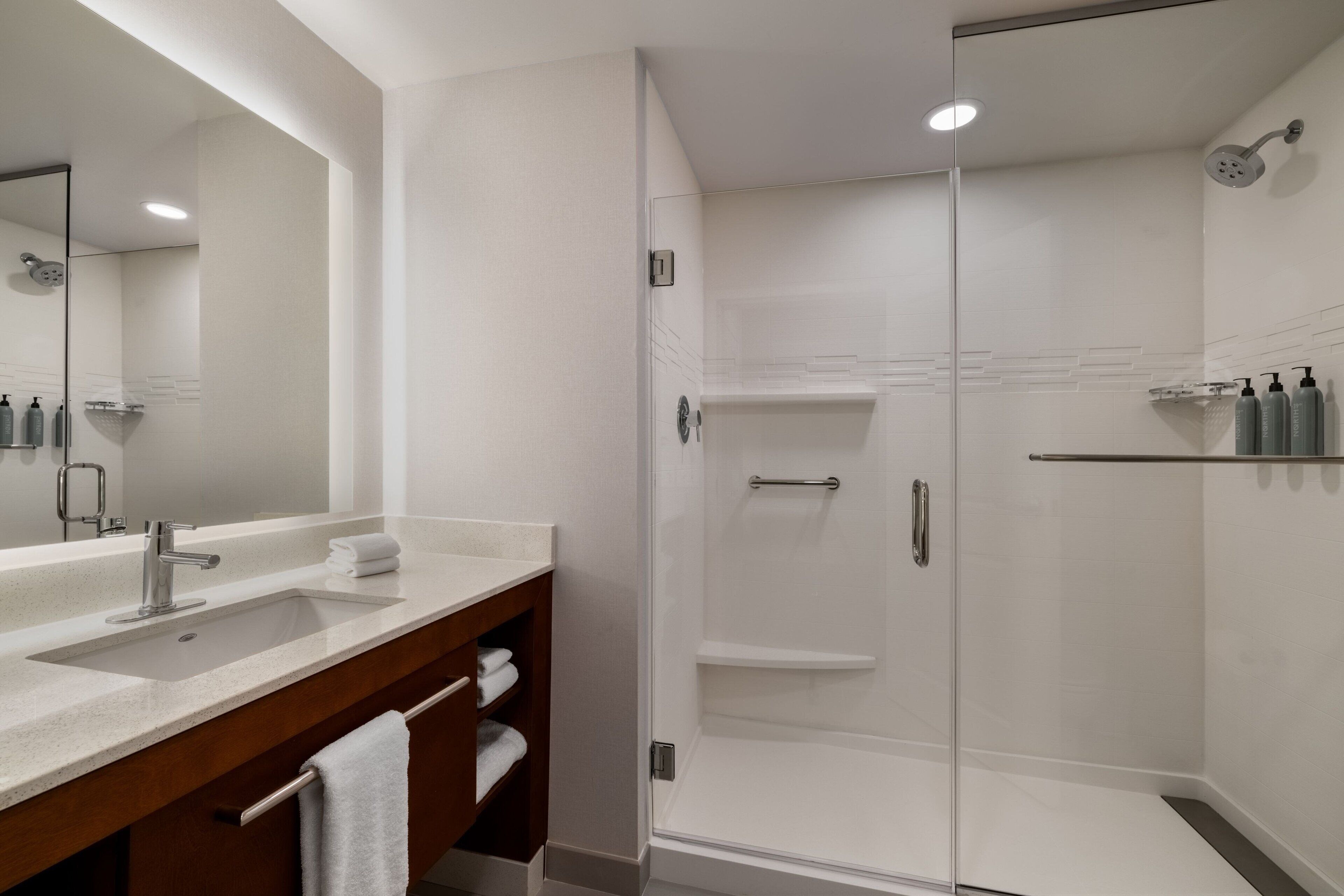 A modern bathroom with a large mirror, a sink, a shower, and a vanity with a towel rack.