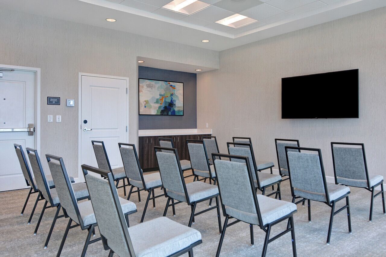A conference room with grey upholstered chairs, a flat-screen TV mounted on the wall, and a door with a sign indicating room number 27.