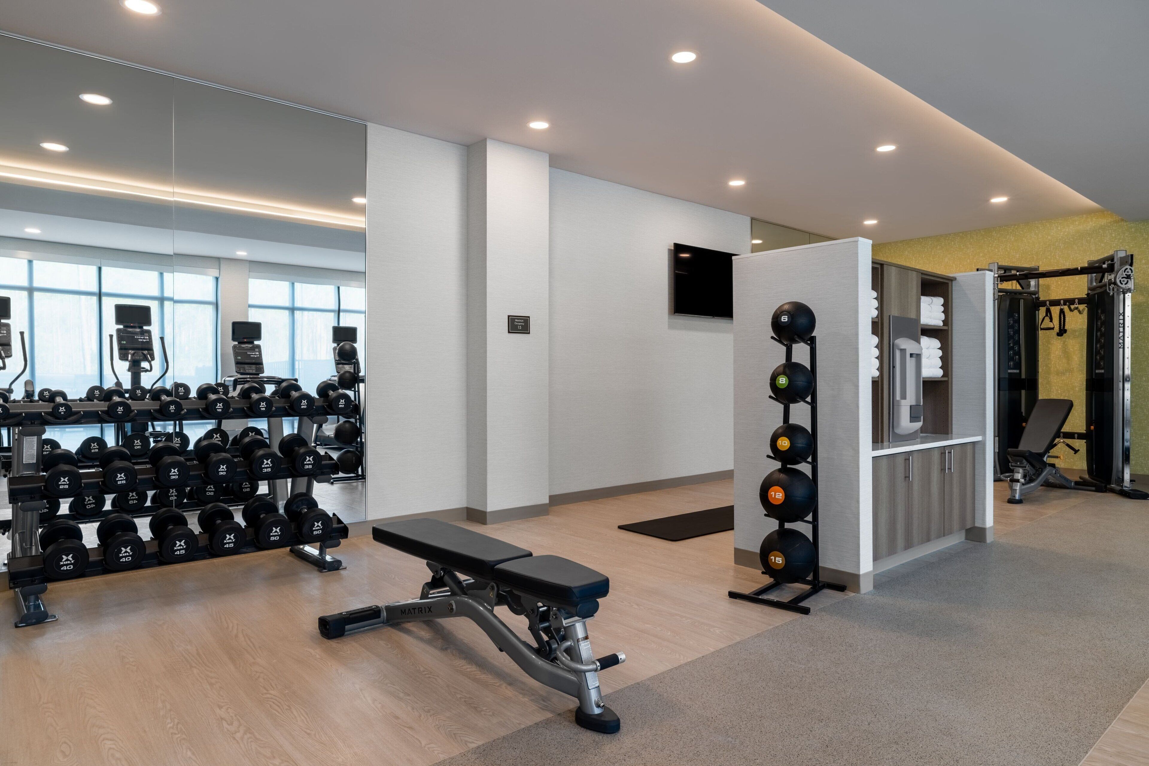 A gym with weightlifting equipment, a bench, and a mirror reflecting the space.
