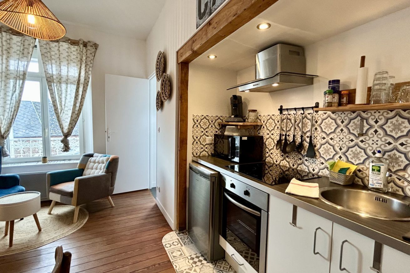 A compact kitchen with modern appliances, a dining area with a round table and chairs, and a window with curtains.
