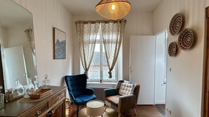 A room with a wooden floor, a large mirror, two chairs, a round table, and a window with curtains. - Belle Échappée, Expérience Unique, Alliant Charme Historique, Commodités Moderne (Le Crotoy)