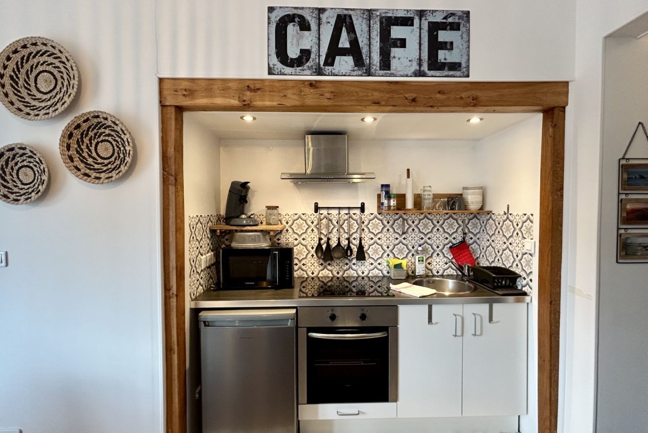 Une cuisine compacte avec un plafond orné de poutres en bois, un four à micro-ondes, un lave-vaisselle et un four encastré.